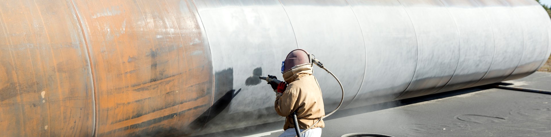 Worker manually sandblasting a large pipe