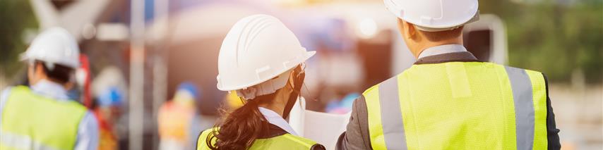 business people in high visibility vests looking at plans on construction site 