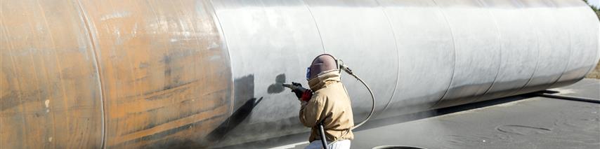 Worker manually sandblasting a large pipe